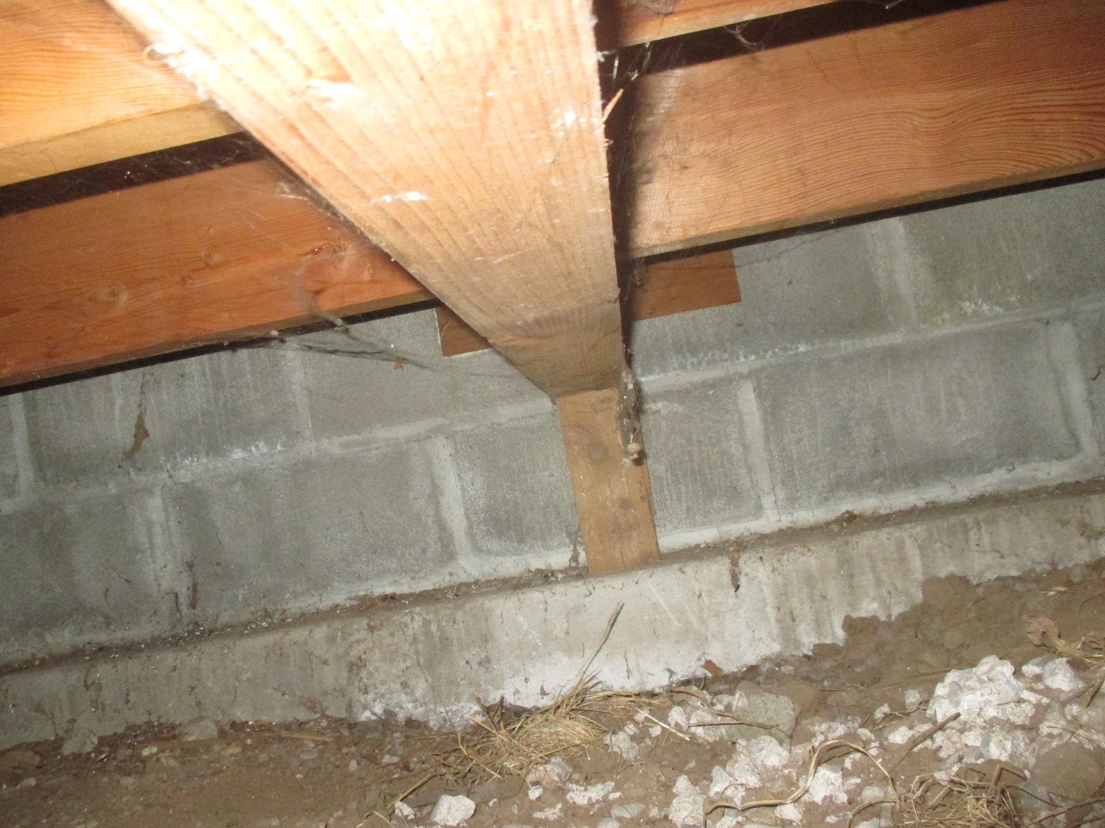Crawlspace view of a concrete block foundation wall with a wood post and floor beam at an older house