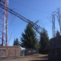 Collapsed guyed tower hanging in the guy wires of a damaged tower above an equipment shelter near Lyons