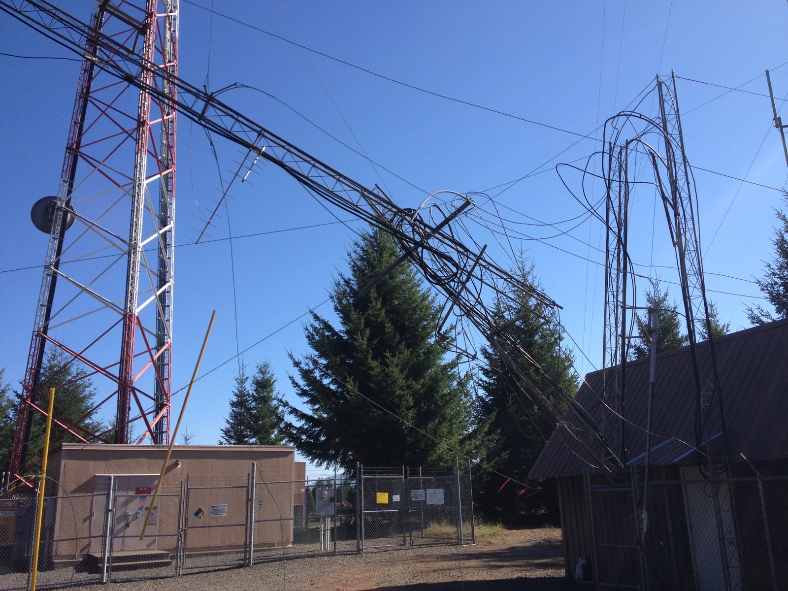 Collapsed guyed tower hanging in the guy wires of a damaged tower above an equipment shelter near Lyons