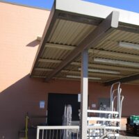 Steel-framed canopy over a grocery store loading dock against a tan masonry wall