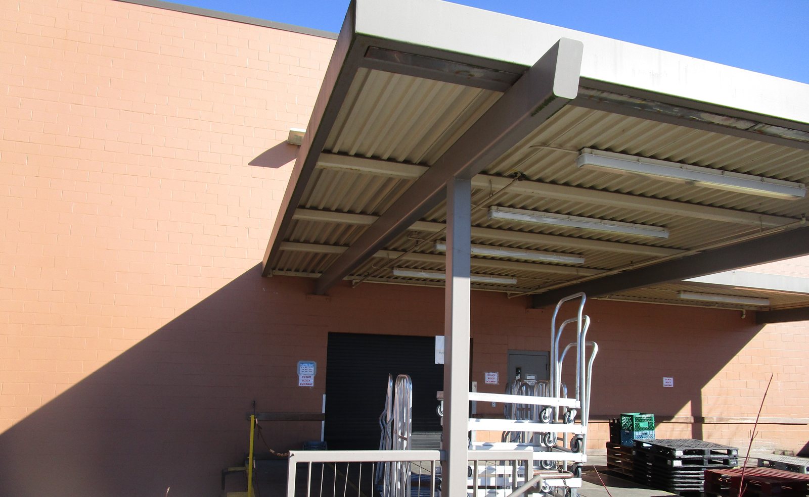 Steel-framed canopy over a grocery store loading dock against a tan masonry wall