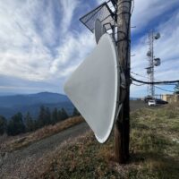 Microwave dish mounted on the aging wood pole, with forested Coast Range ridges beyond