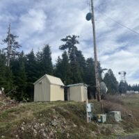Wood antenna pole with dishes beside two small equipment shelters on the Marys Peak ridgetop