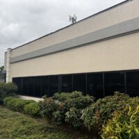 Long side of a one-story tan office building with a band of dark windows above landscaped shrubs, Eugene